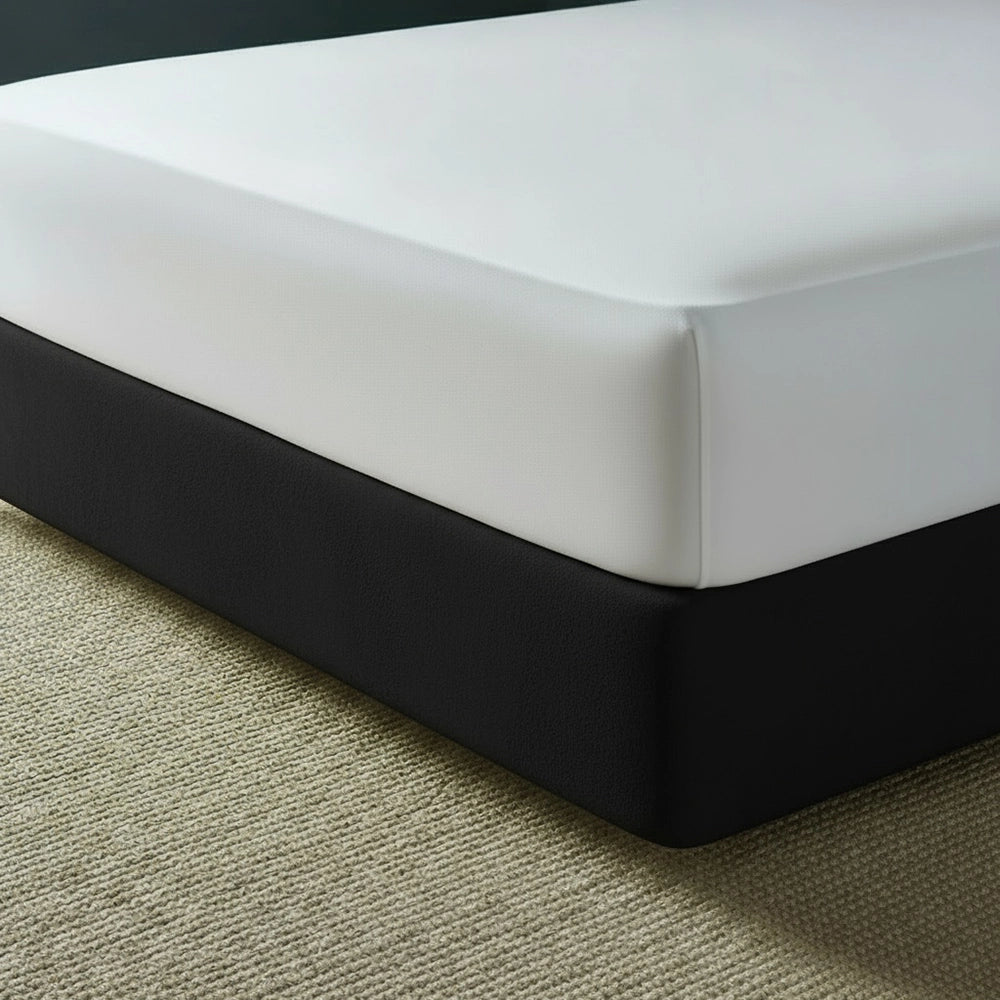Black mock suede base wrap covering bed base with white fitted sheet on beige jute mat—luxury bed base cover by Linen & Co