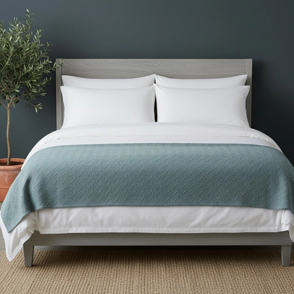 Luxury white cotton bedding set with duck egg blue quilted throw blanket on grey wood bed frame, styled with beige jute mat and olive plant—premium South African linens by Linen & Co for hospitality and residential use