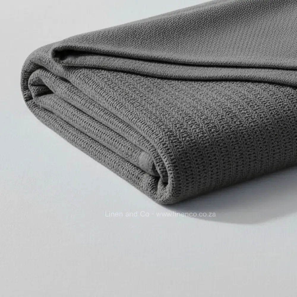 dark grey cotton cellular blanket with textured waffle weave draped over white bed, showing soft fabric texture and quality craftsmanship—breathable bedding by Linen & Co