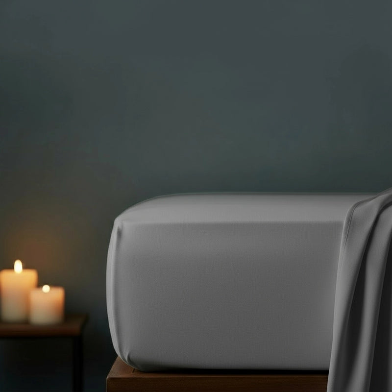 Grey fitted sheet on bed with candlelight ambiance against moody dark grey wall—premium cotton percale fitted sheet by Linen & Co