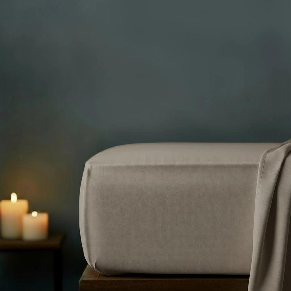 Stone fitted sheet on bed with candlelight ambiance against moody dark grey wall—premium cotton percale fitted sheet by Linen & Co