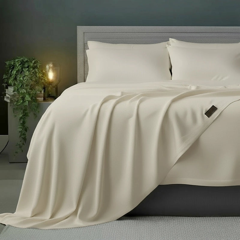 Cream flat sheet draped over grey bed frame with white pillows, styled with olive plant and bedside lamp against moody dark teal-grey wall—premium cotton percale flat sheet by Linen & Co