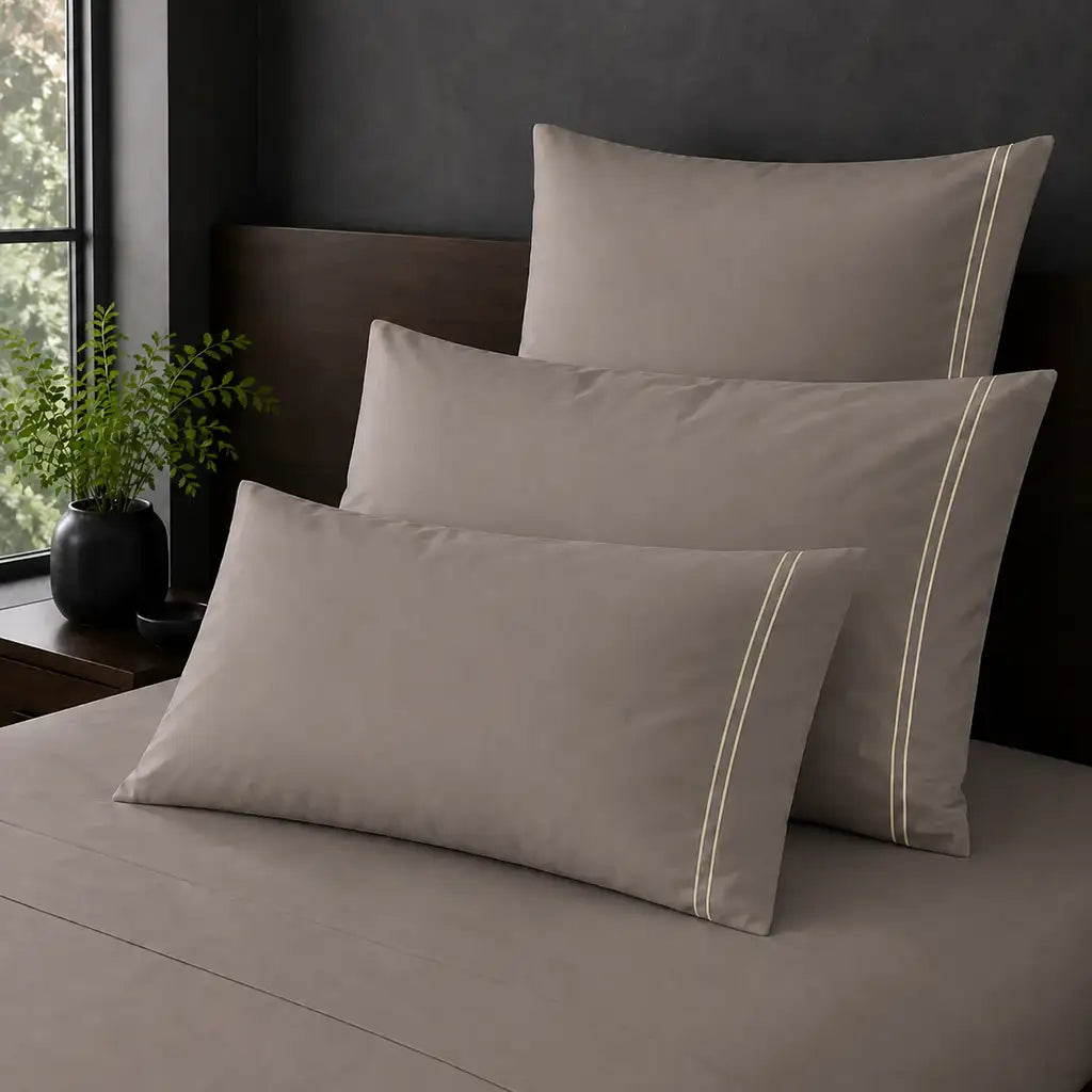 Stone Polycotton Percale 200TC Standard, King and Continental pillowcases on a bed with two row  Cream satin stitch.