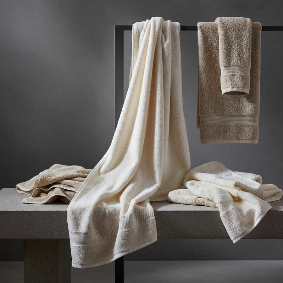 Towels draped and folded in white and stone tones on bench by Linen and Co - custom sizing guide for luxury bath linens
