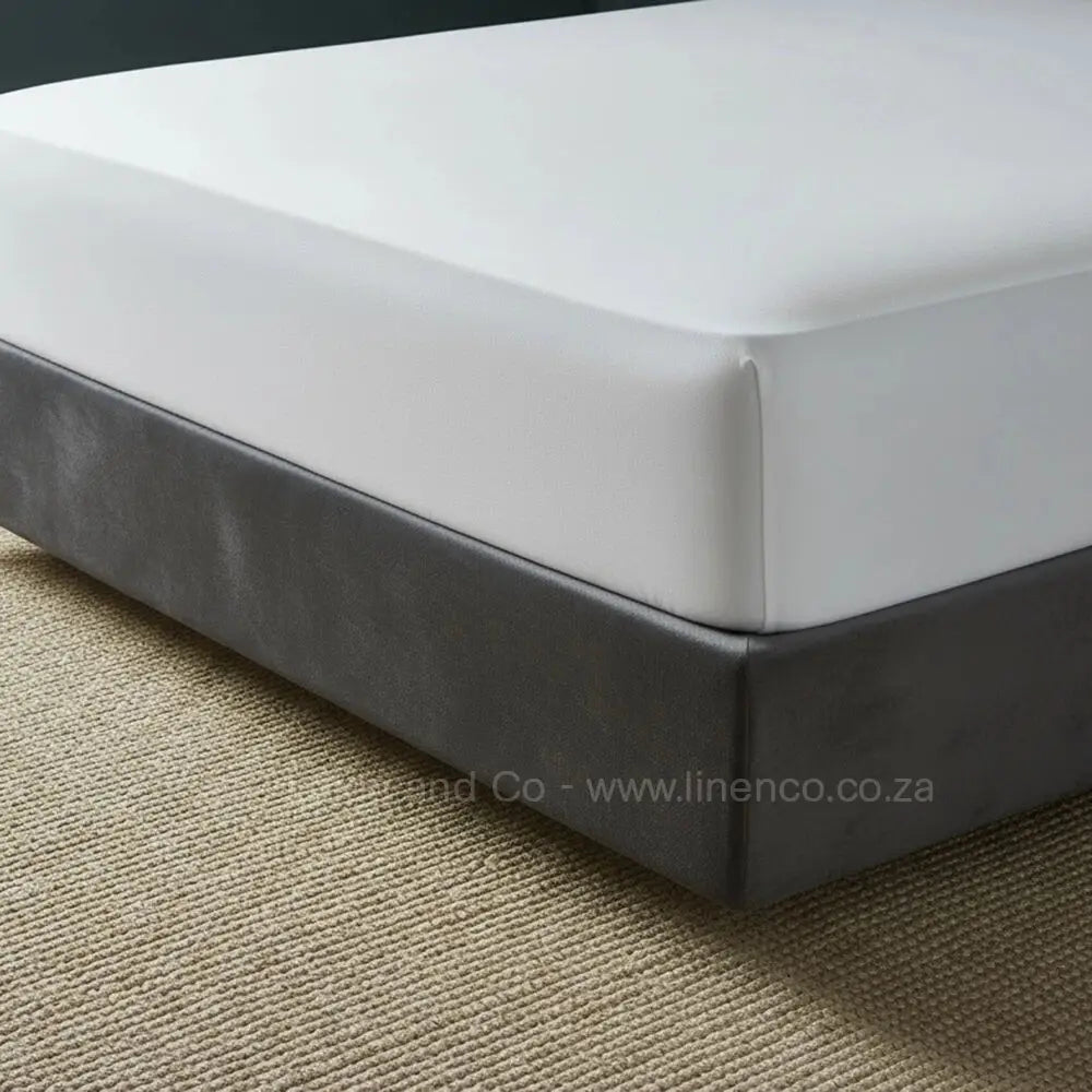 White fitted sheet with deep pocket elastic displayed on charcoal bed frame with neutral textured rug, showcasing premium hospitality-grade bedding by Linen & Co
