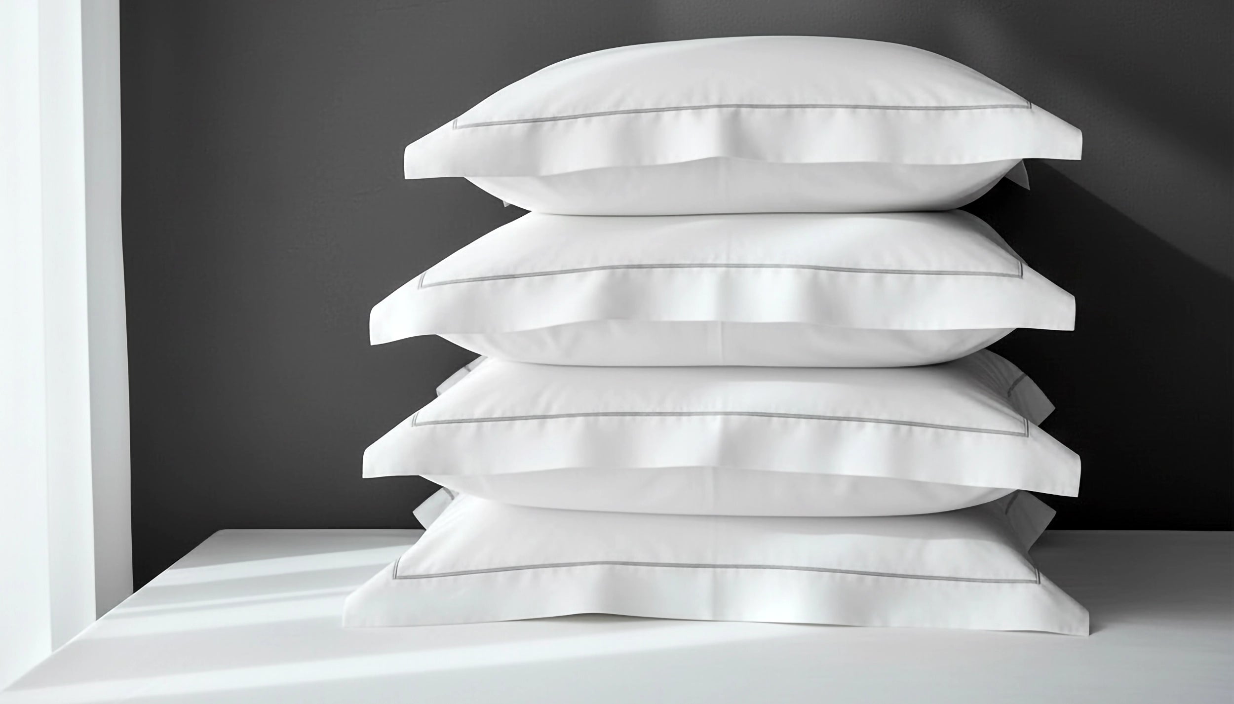 White Oxford satin stitch pillowcases stacked on a grey background by Linen and Co - premium hospitality pillowcases for hotels and guest houses
