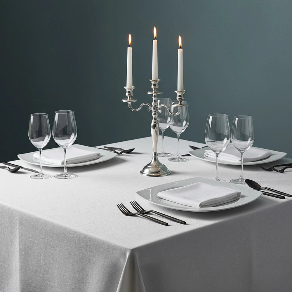 Elegant white square tablecloth on formal dining table set with white napkins, place settings, black cutlery, wine glasses, and silver candelabra against moody dark backdrop—luxury table linens by Linen & Co for hospitality and events