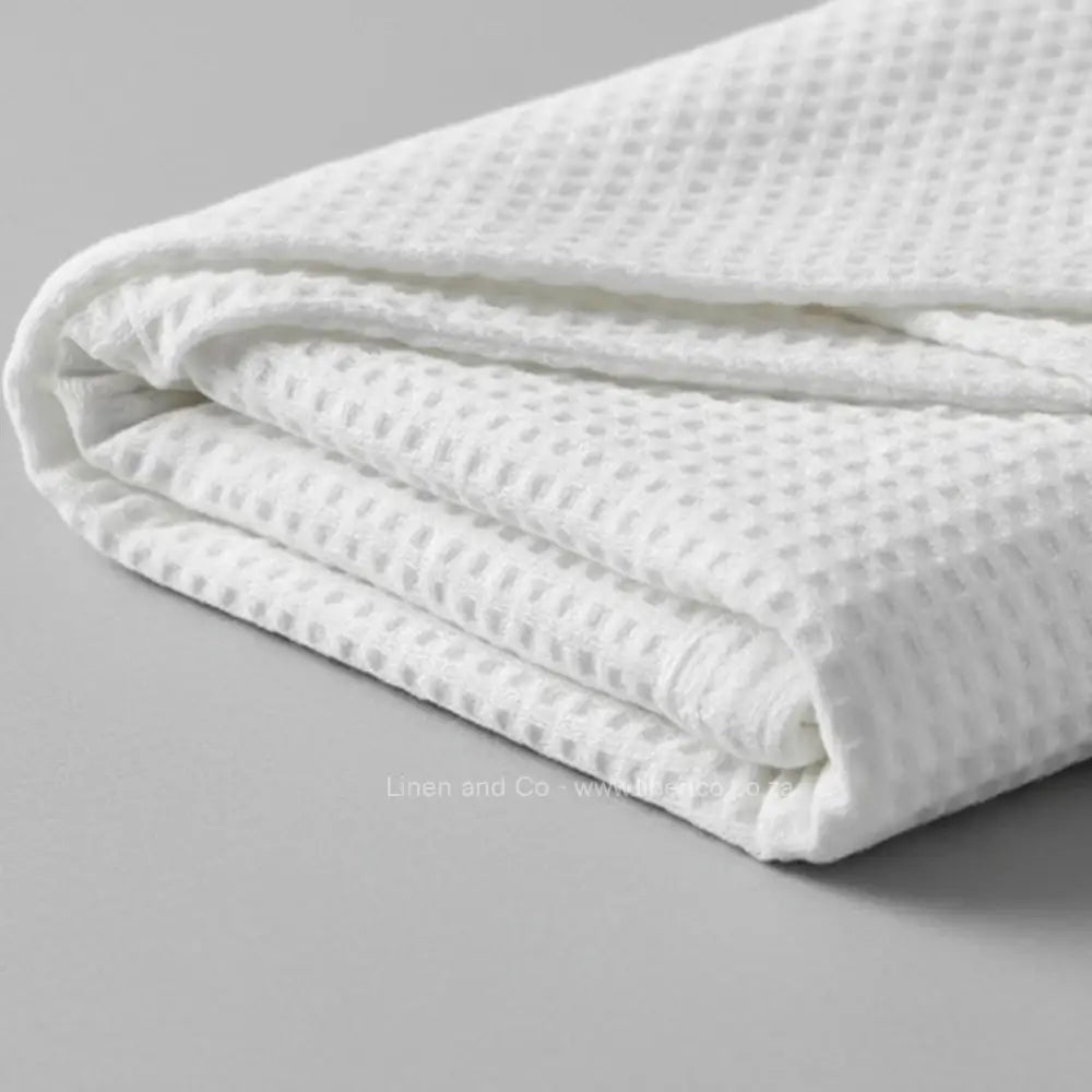 white cotton cellular blanket showing textured waffle weave fabric on neutral grey background—soft, breathable bedding by Linen & Co